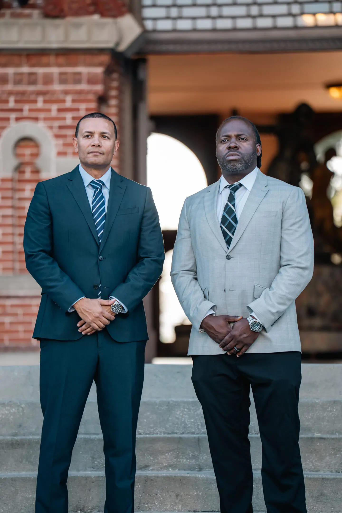 Two men in formal attire standing confidently outdoors.